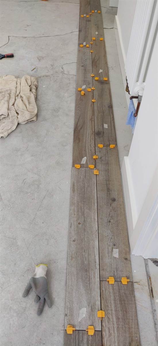 During — first row of wood-effect floor tiles laid and clipped level along the wall
